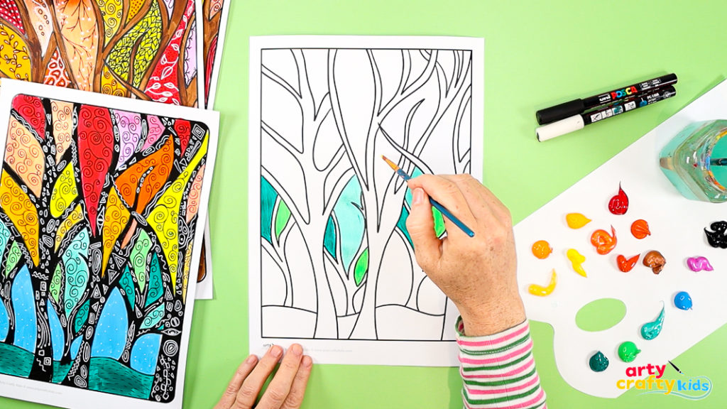 painting foliage sections of a fall tree art template with bright paints, surrounded by finished examples.