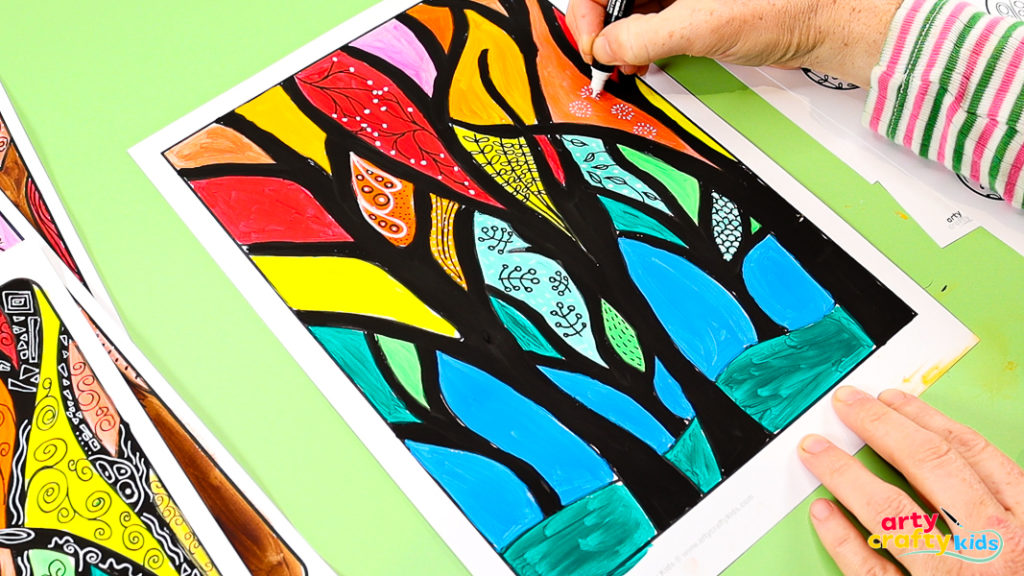 Hand using a marker to add doodle patterns onto colorful fall tree painting with black trunks